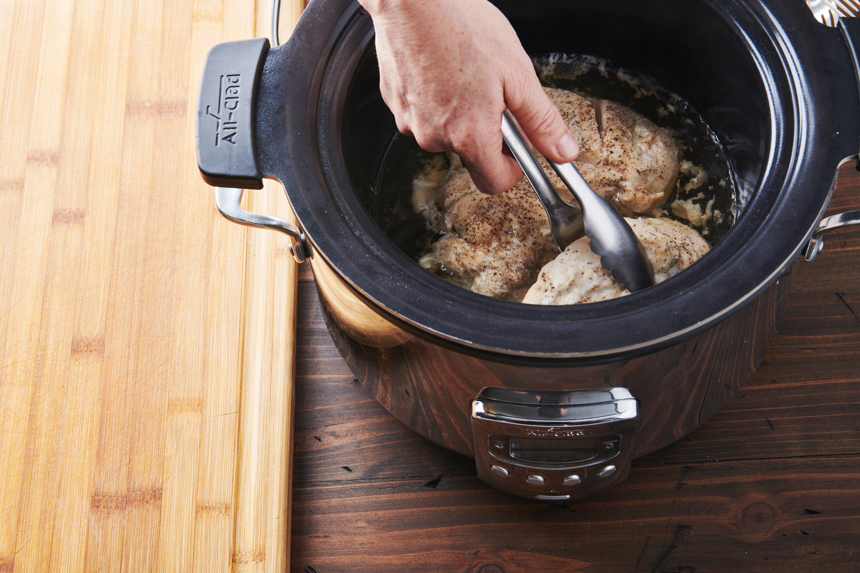 Tongs pulling chicken from a slow cooker.
