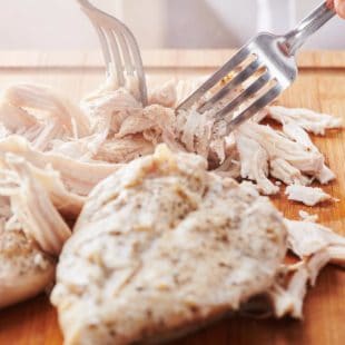 Partially-shredded chicken breasts with two forks.