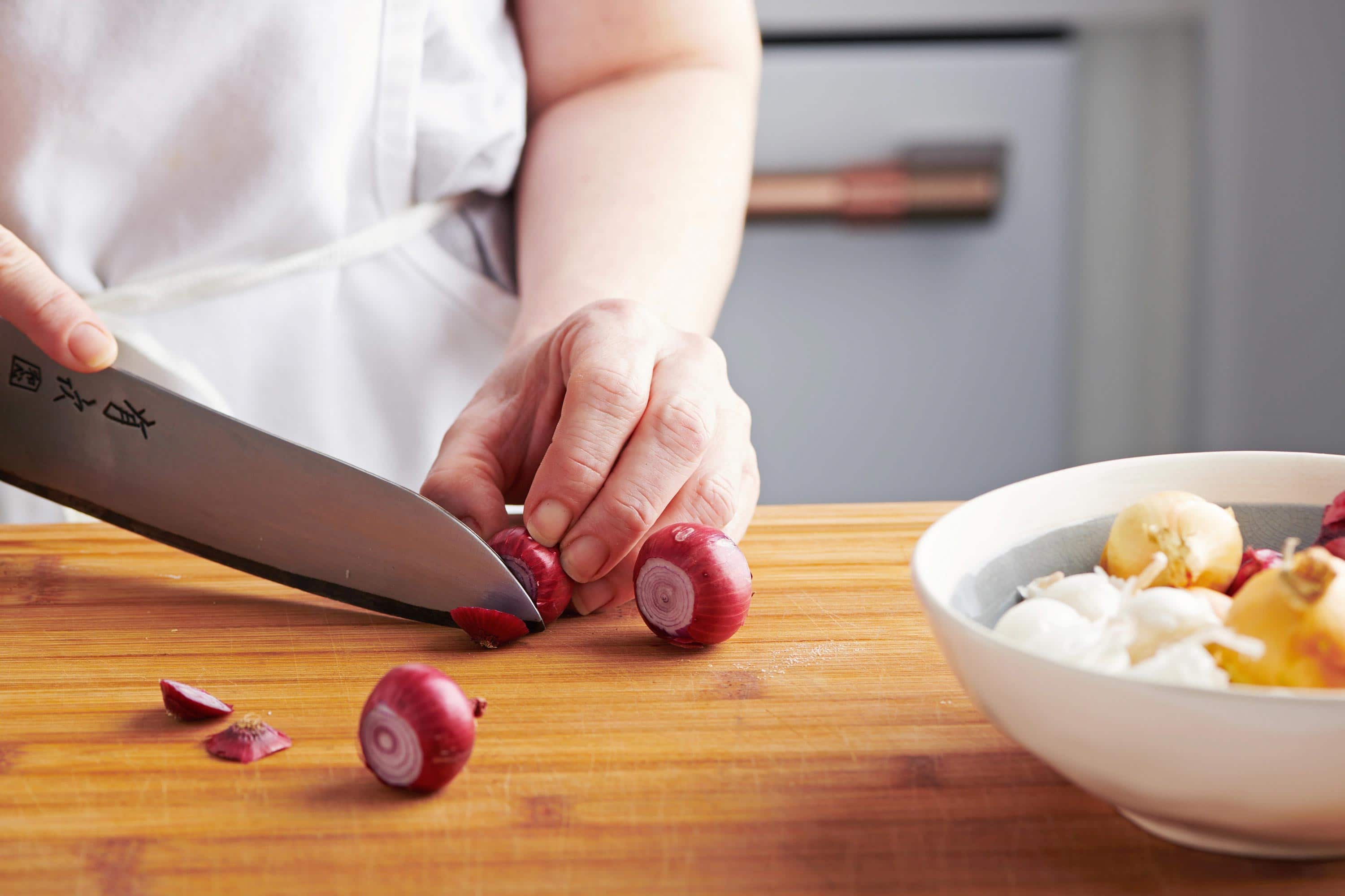 Woman cutting the end off of a red pearl onion.