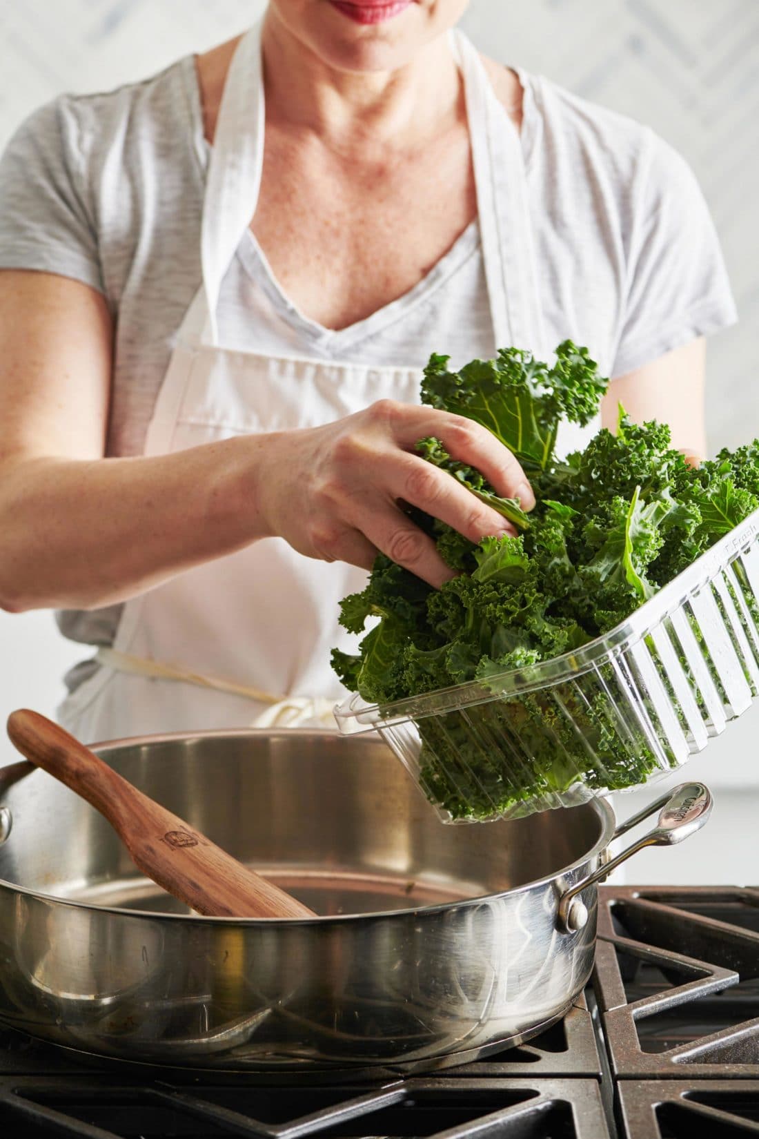 Woman adding Kale to a pan of oil and garlic.