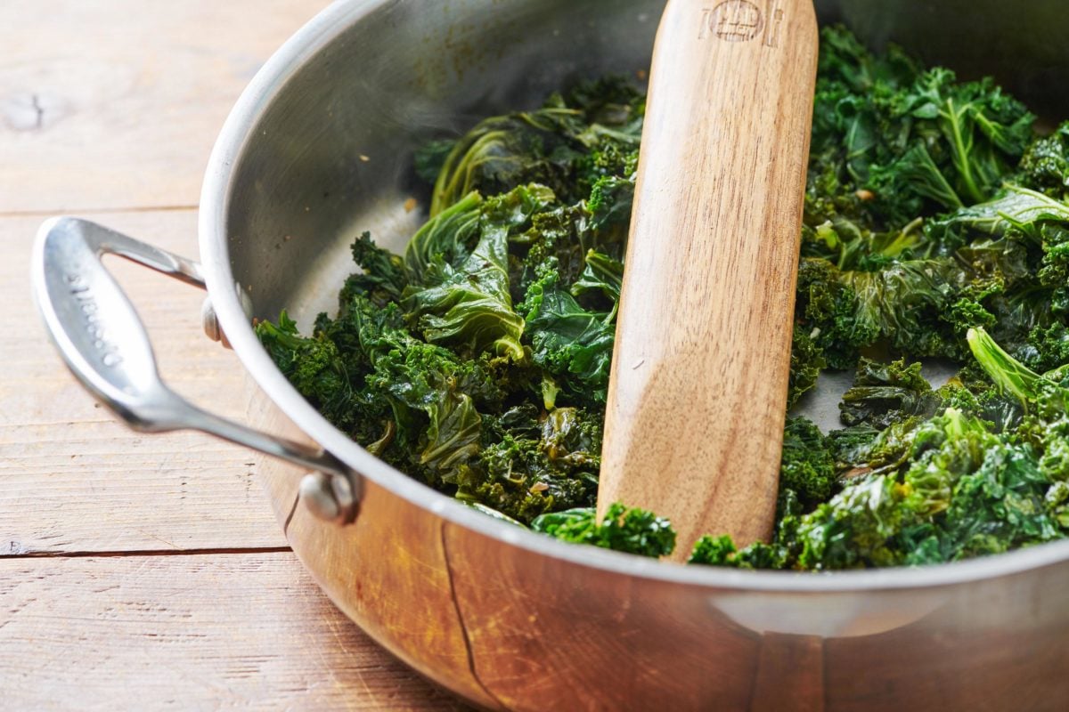 Cooked Kale in a pan with a wooden spatula.