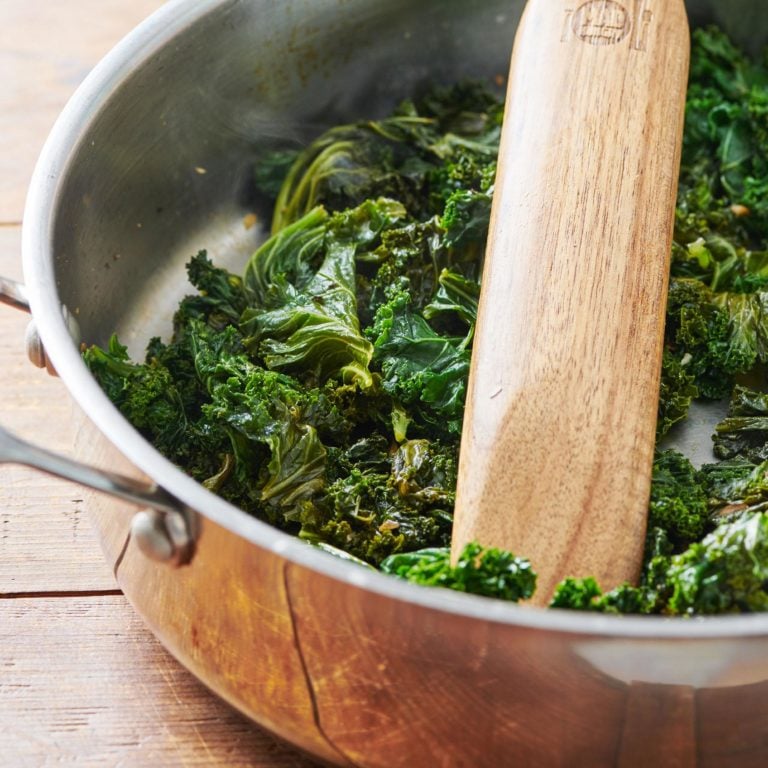 Cooked Kale in a pan with a wooden spatula.