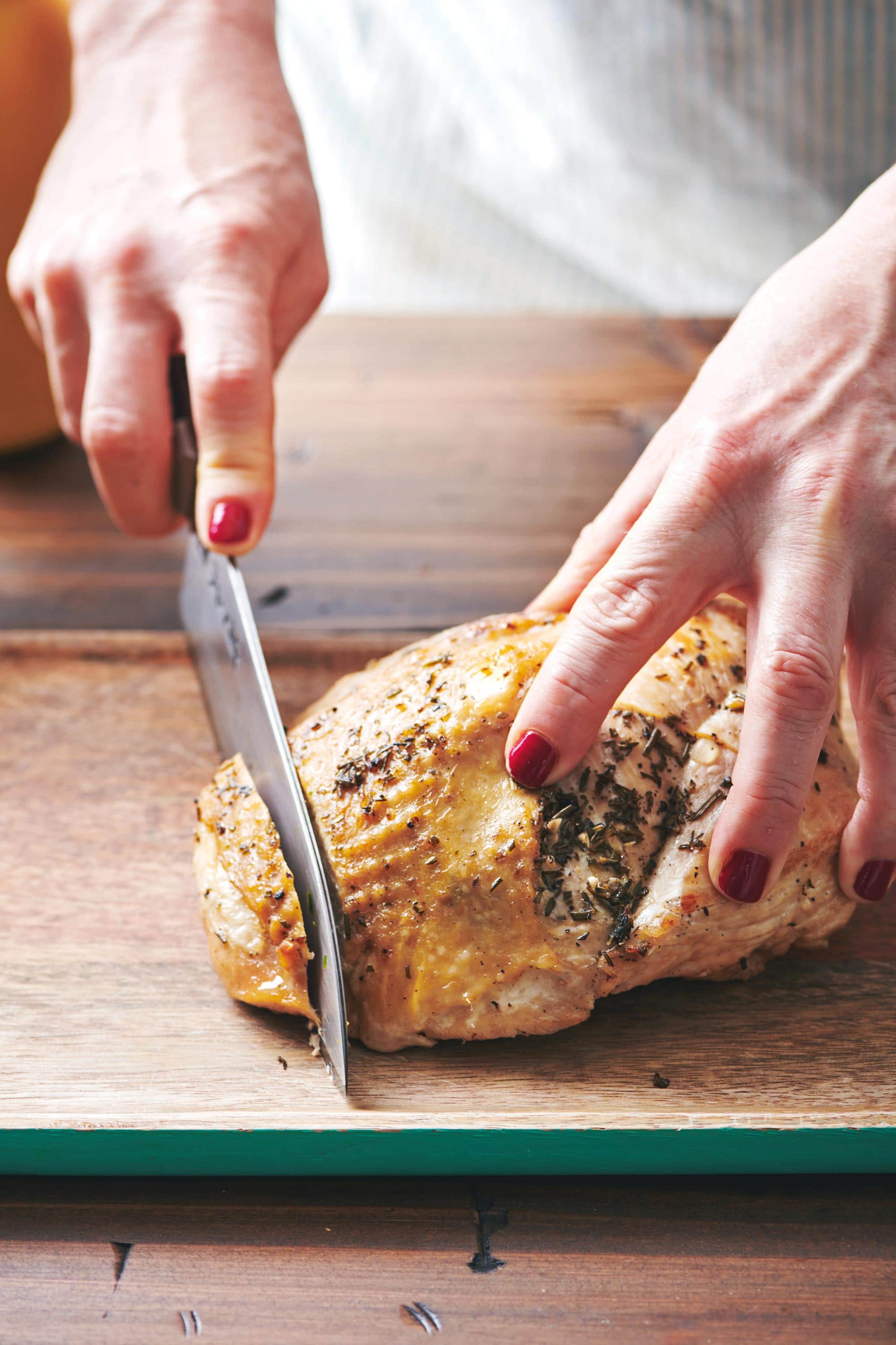 Woman slicing a Turkey Breast with a knife on a wooden surface.