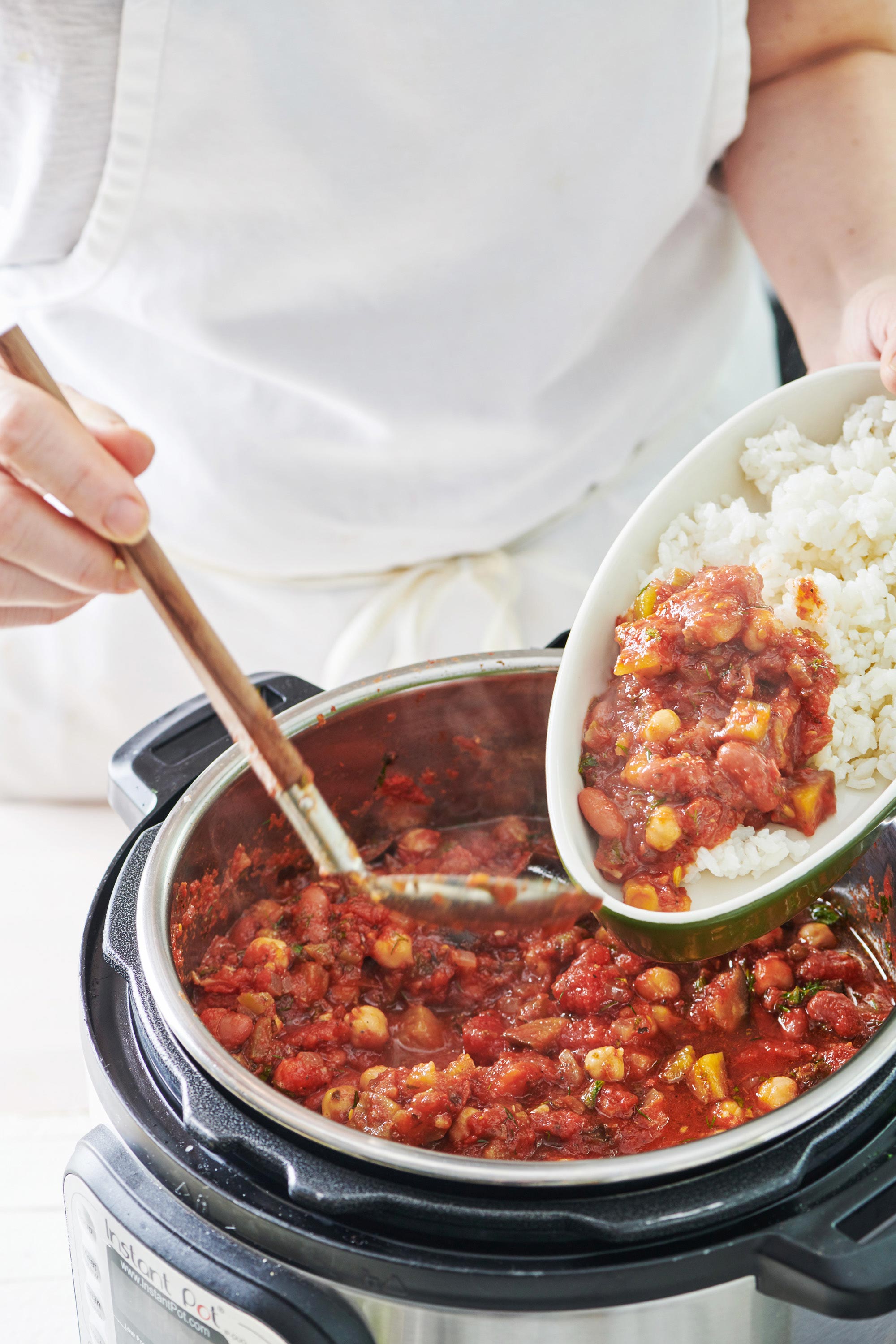 Ladle scooping Vegetable Chili onto plates of rice.