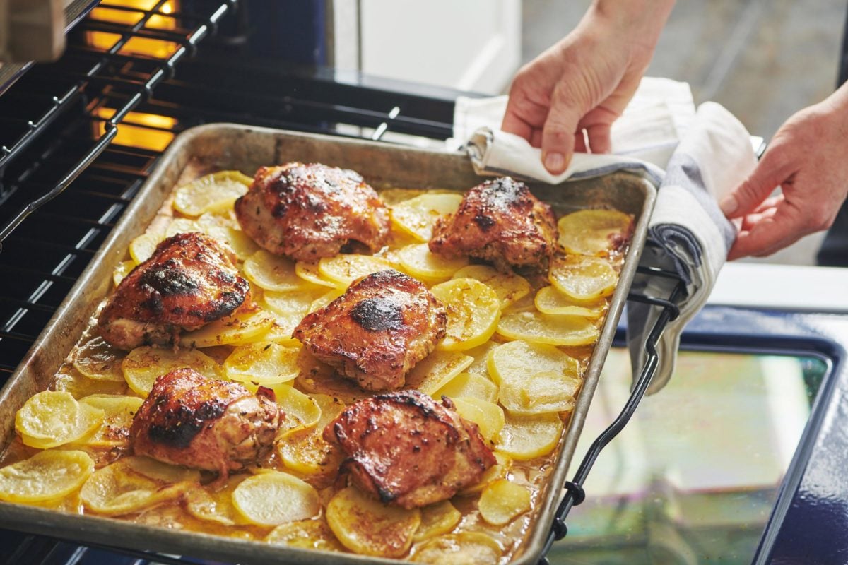 Woman pulling a baking sheet of Roasted Marinated Chicken and Potatoes from the oven.