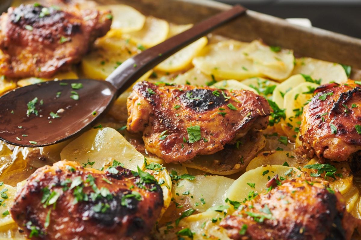 Spoon resting on a baking sheet of Roasted Marinated Chicken and Potatoes.