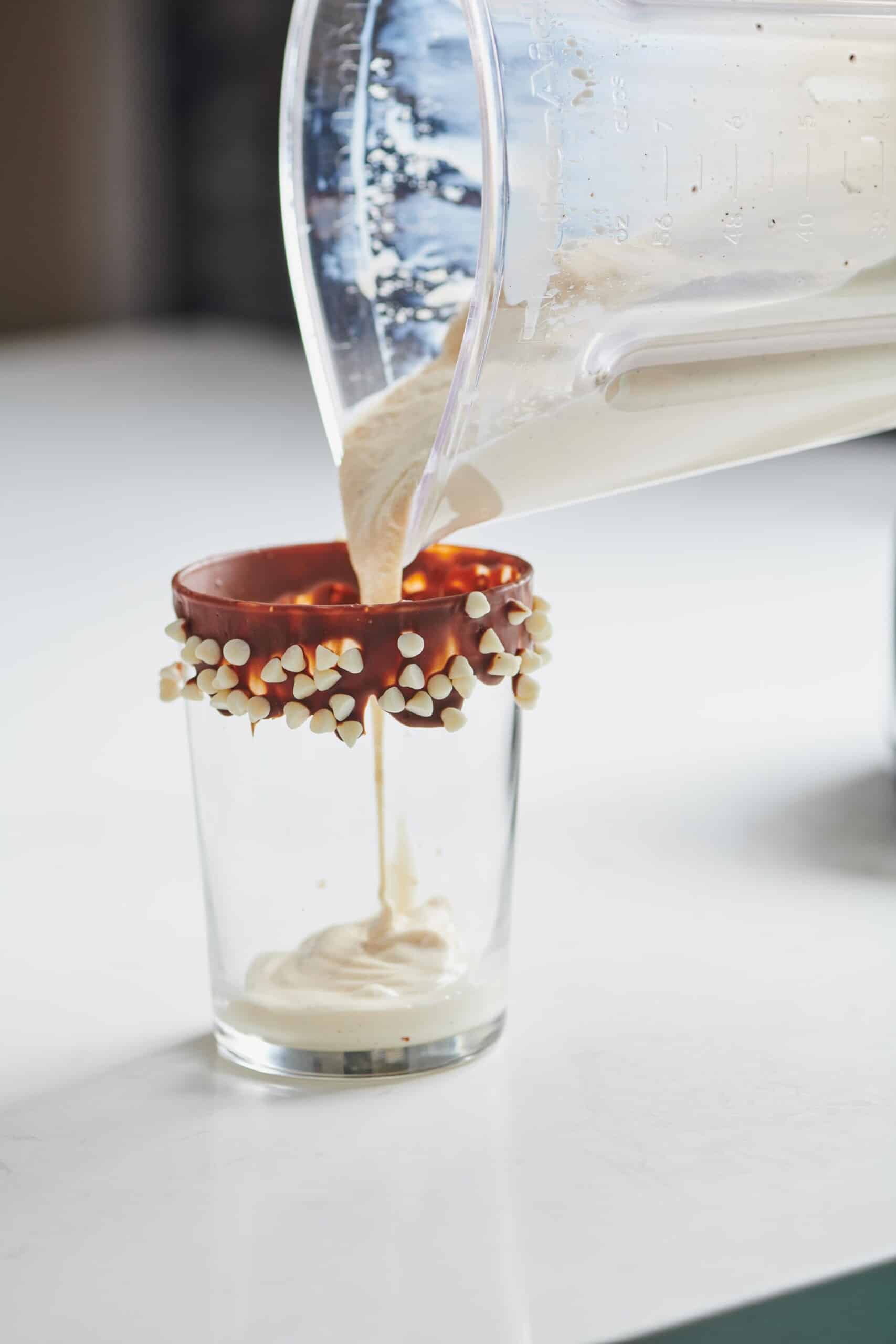 Pouring eggnog milkshake into a glass with a chocolate and chocolate chip rim.