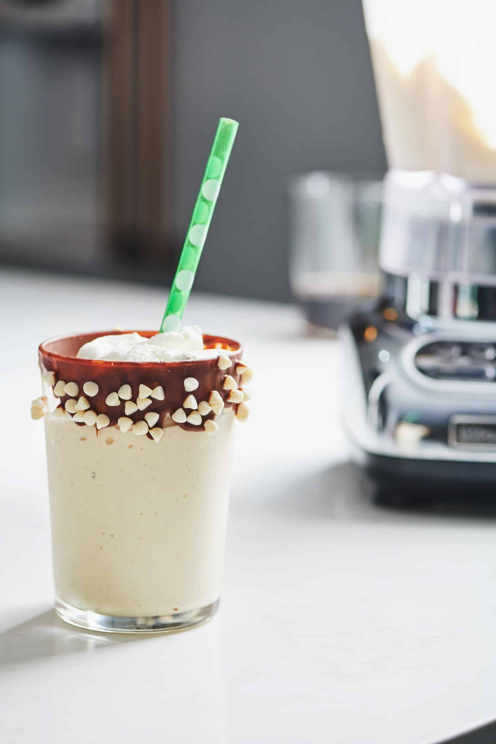 Glass of vanilla egg nog milkshake with a green straw.