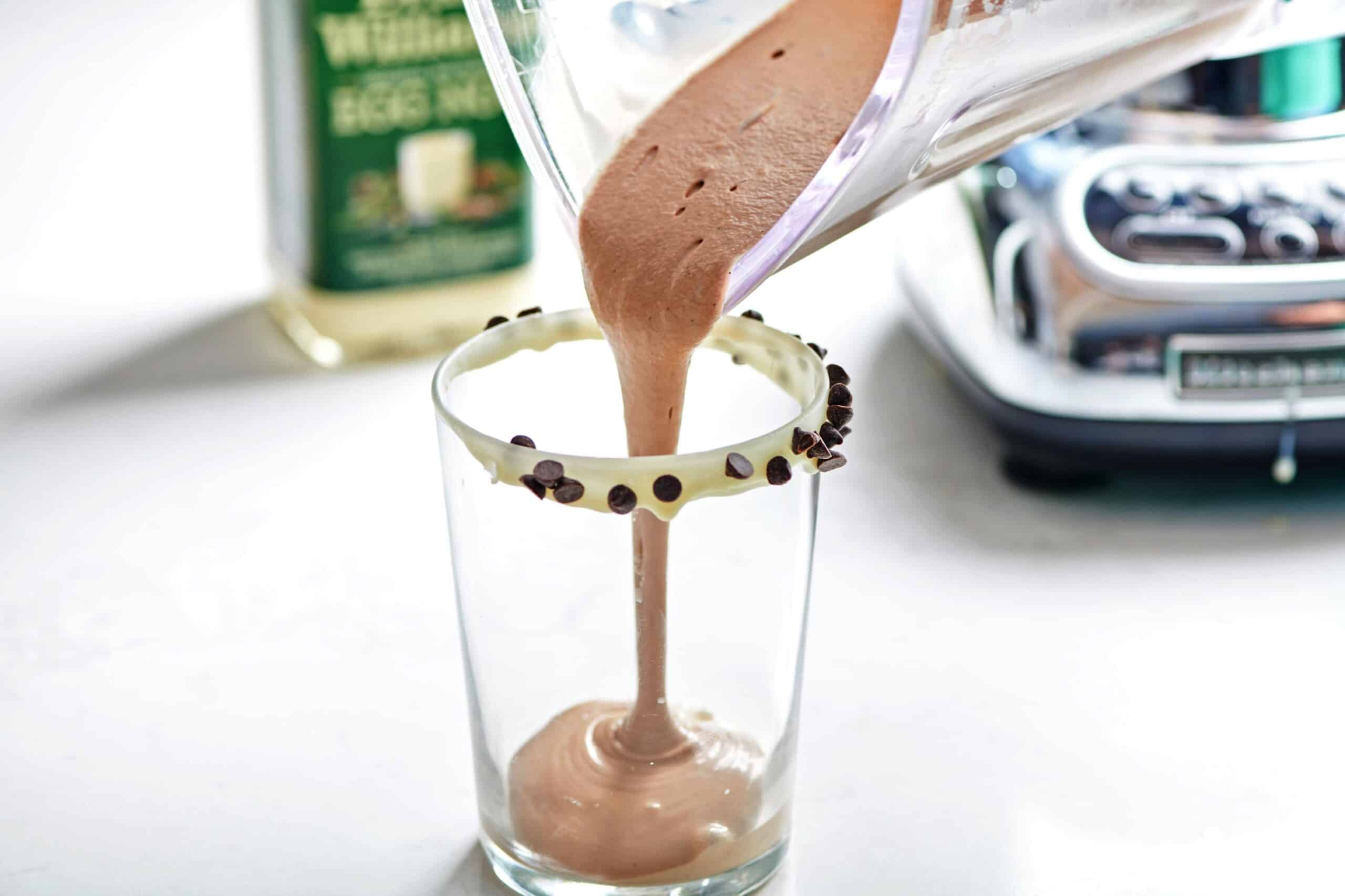 Pouring chocolate eggnog milkshake into glass from blender pitcher.