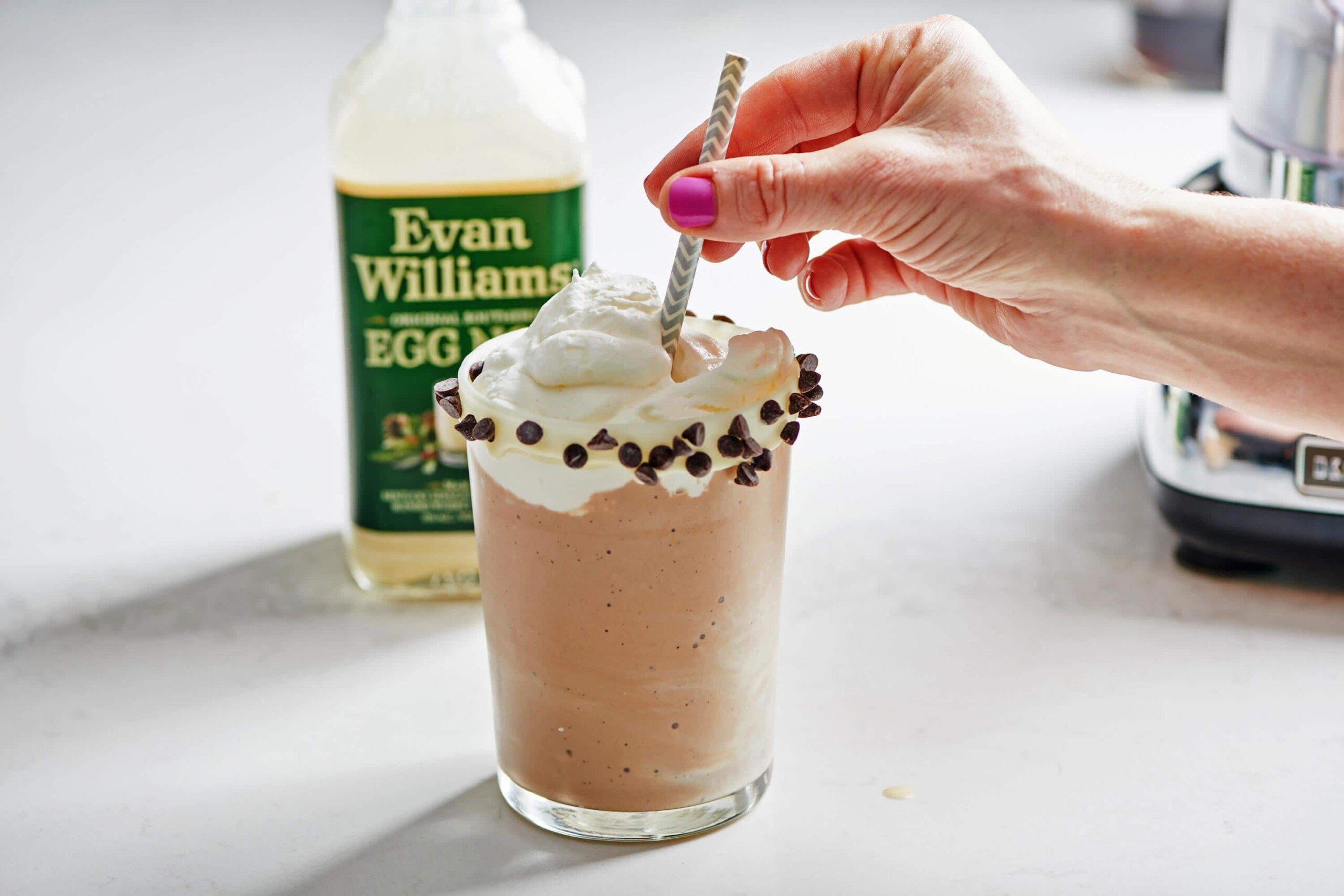 Woman placing a straw into an egg nog milkshake topped with whipped cream.