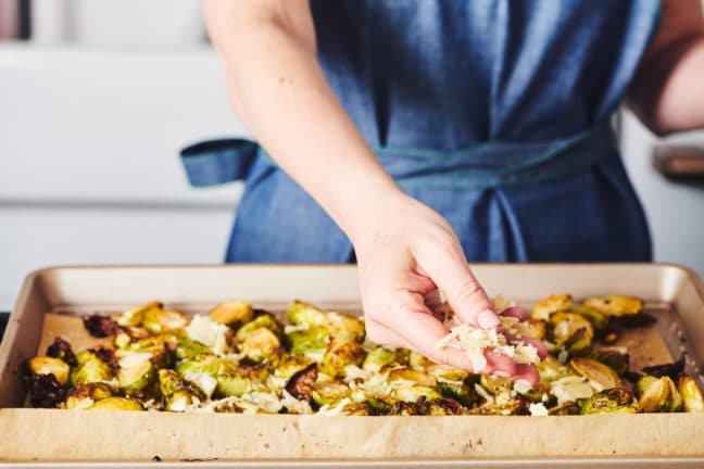 Woman sprinkling onto Brussels Sprouts on a lined baking sheet.