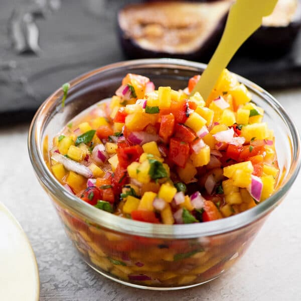Small glass bowl with peach and roasted pepper salsa on table.