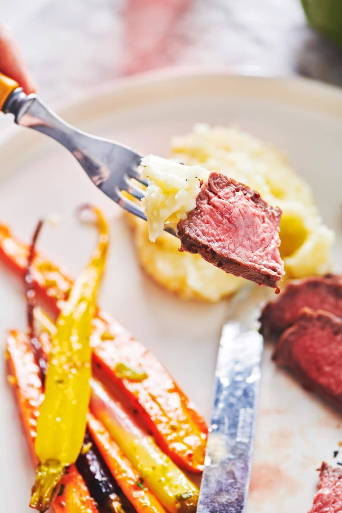 a bite of steak with mashed potatoes on a fork