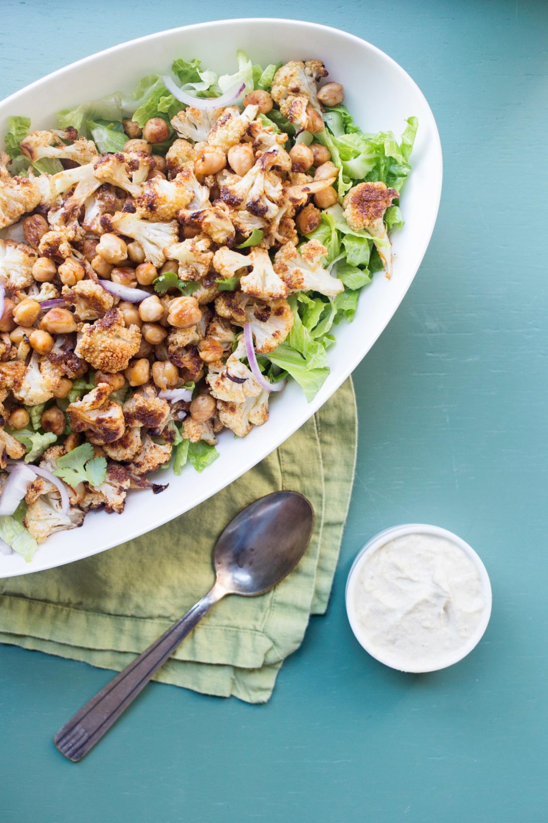 Small bowl of Tahini Dressing next to a plate of Roasted Cauliflower and Chickpea Salad.