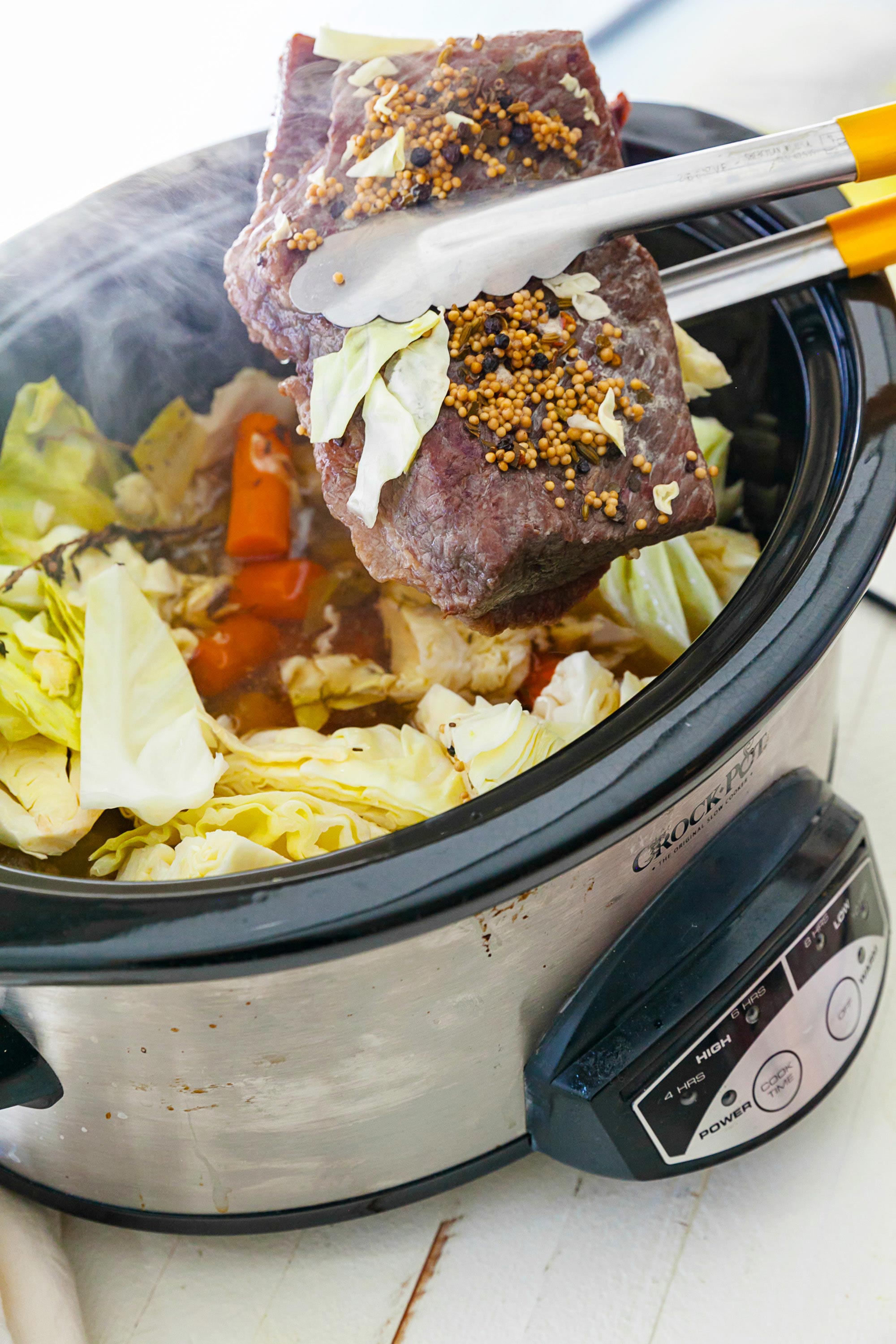Tongs pulling Corned Beef out of a Crock Pot.
