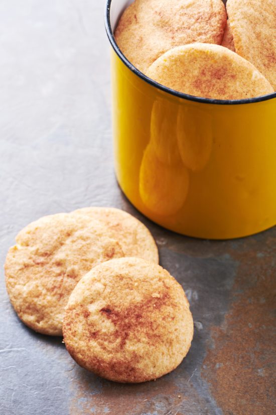 Snickerdoodles in a yellow cookie jar and on a countertop.