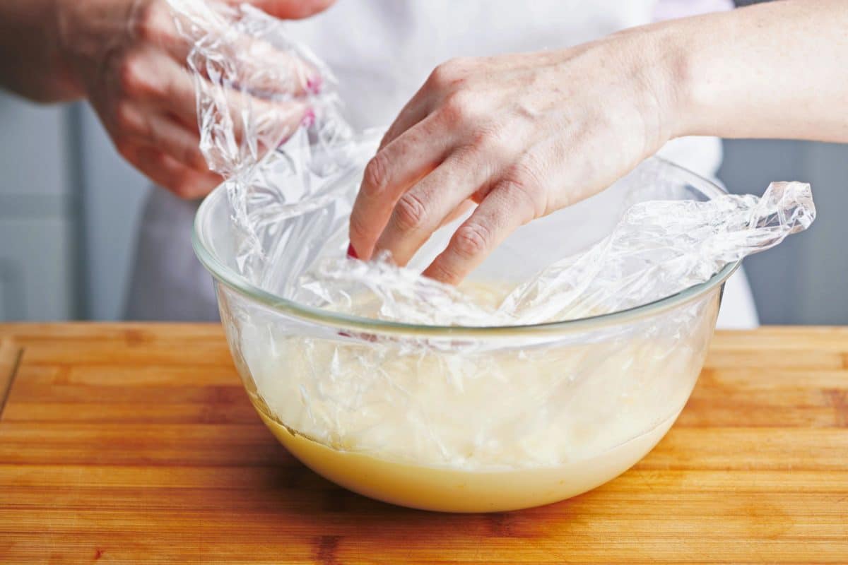 Woman placing plastic wrap on custard in a glass bowl.