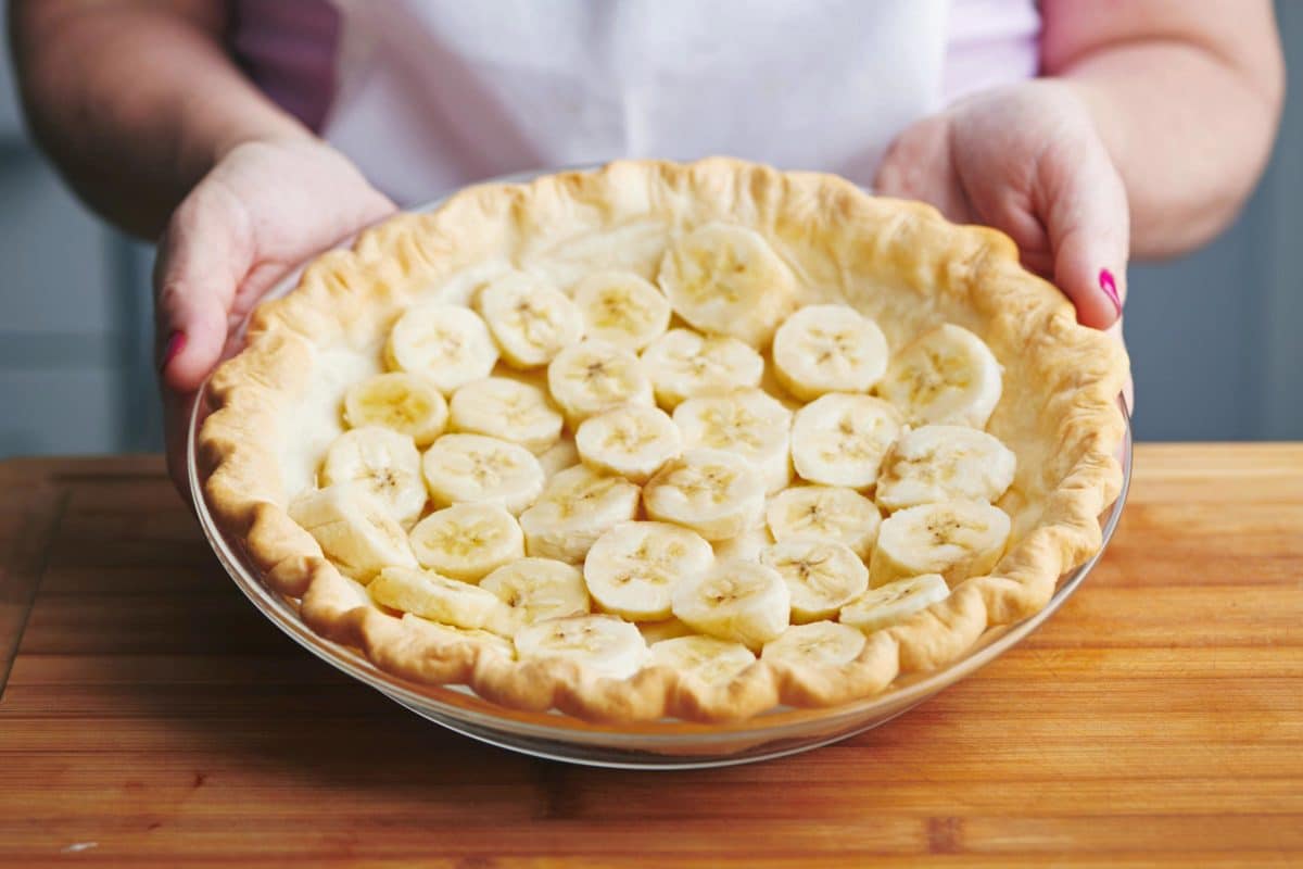 Woman holding a pie crust lined with banana slices.