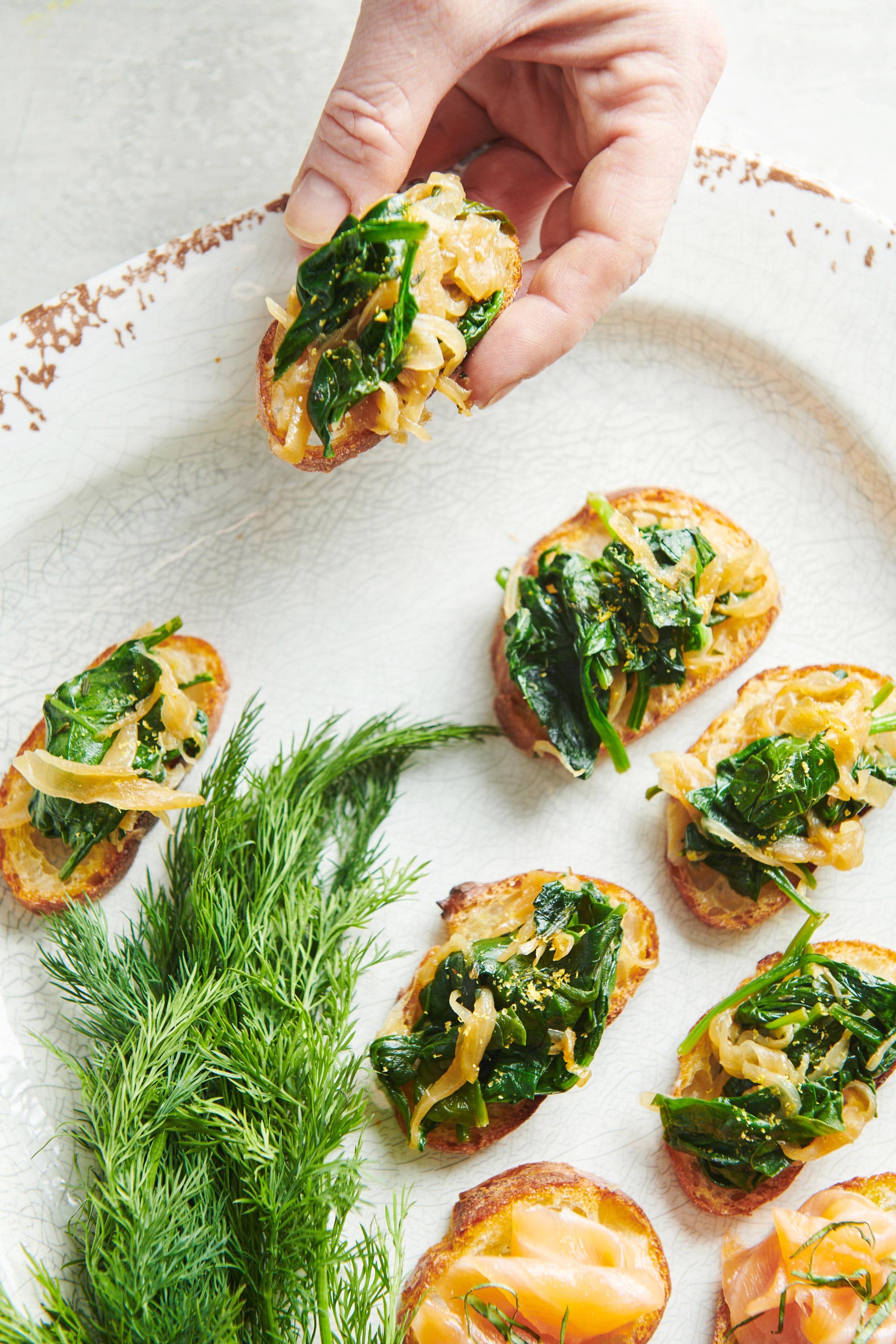 Woman grabbing a Caramelized Onion and Spinach Crostini from a plate.