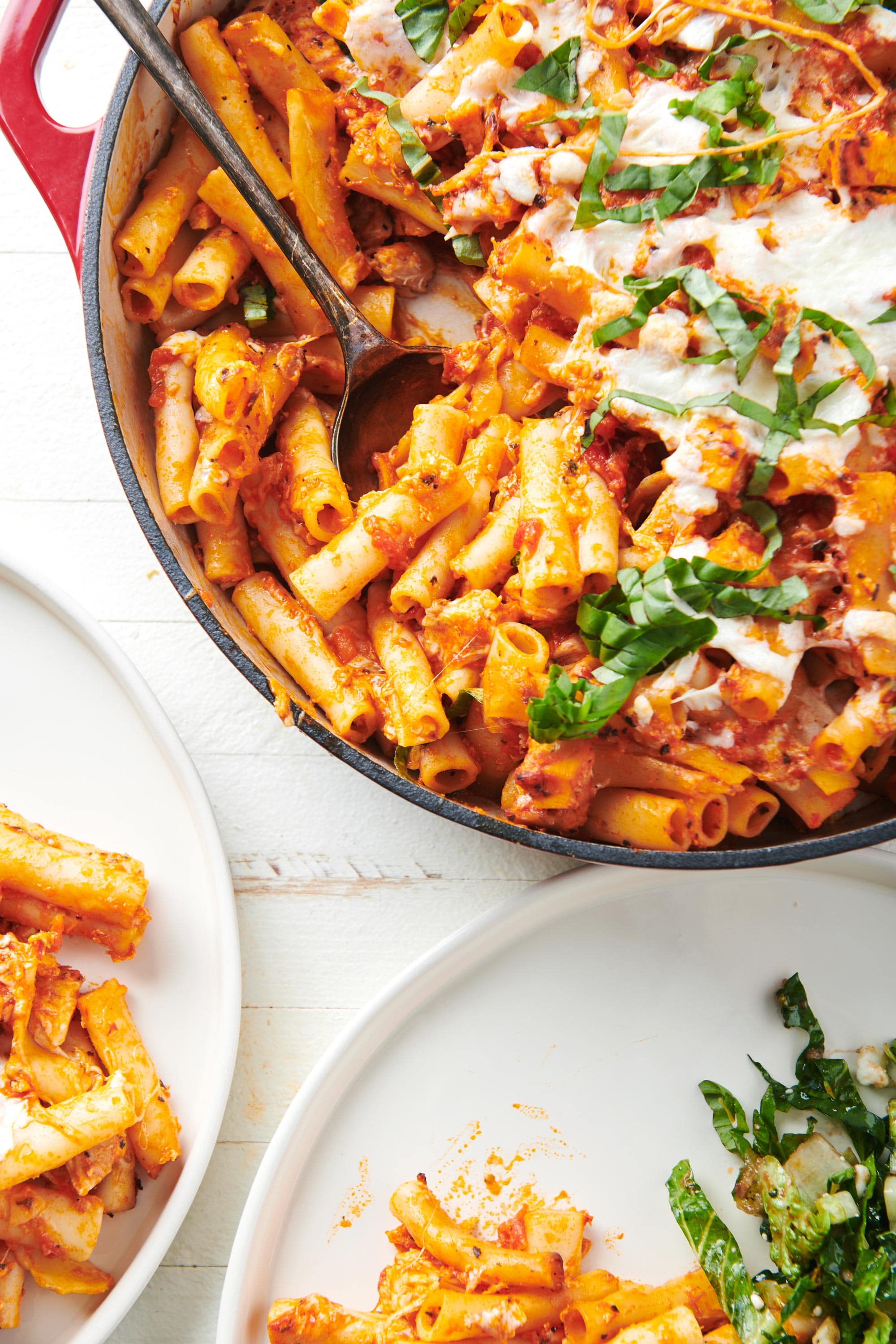 Chicken Parmesan Baked Ziti casserole in Dutch oven with serving spoon and plates.