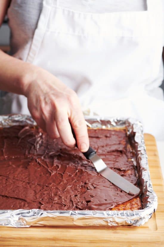 Woman spreading Chocolate on Caramel Matzoh on a lined baking sheet.