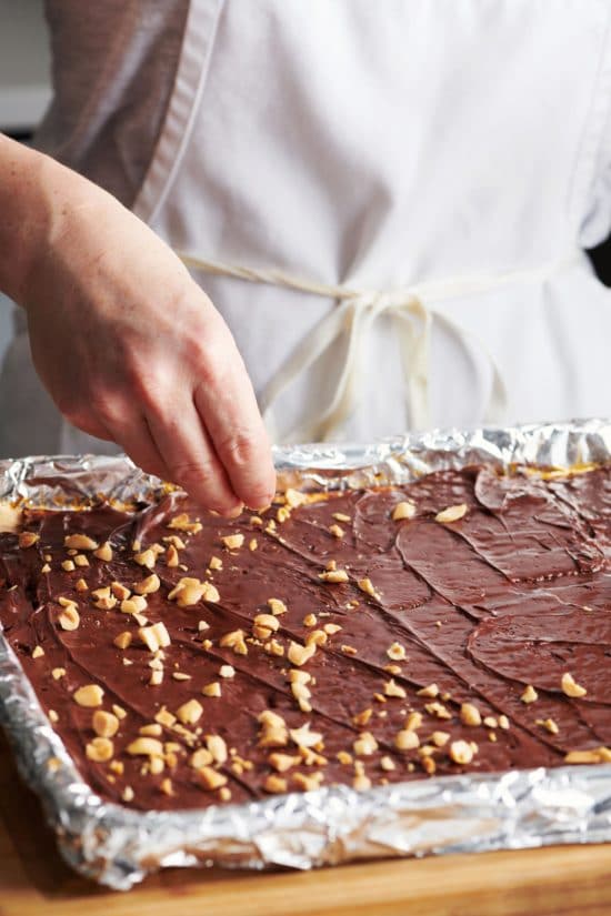 Woman sprinkling peanuts on a baking sheet of Chocolate Covered Caramel Matzoh.