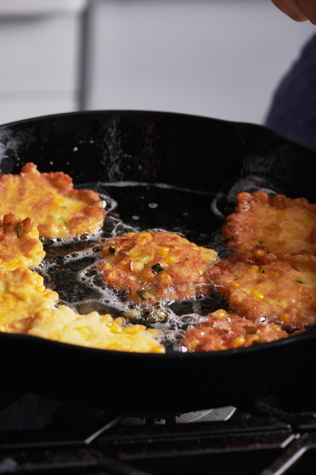 Corn and Zucchini Fritters frying in a skillet.