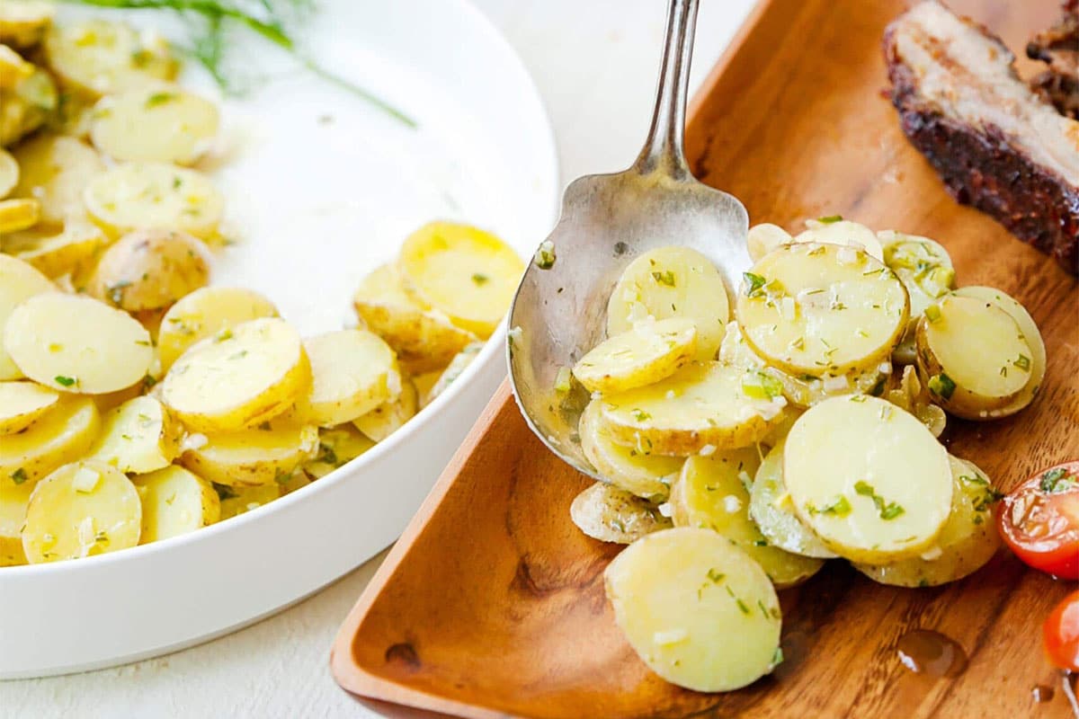 Spoon scooping French Potato Salad onto a wooden plate.