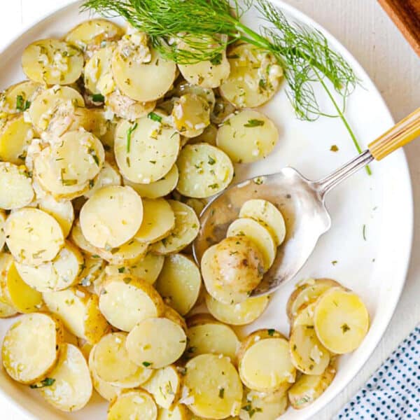 Bowl with French Potato Salad set on a table with utensils and other foods.