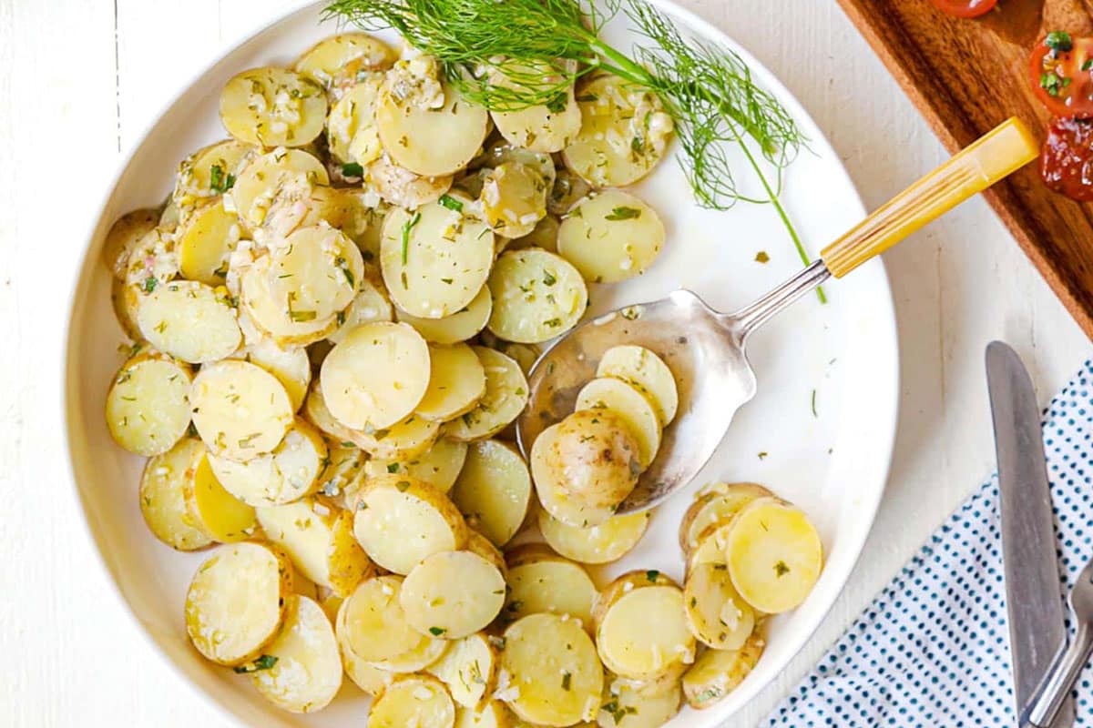 Bowl with French Potato Salad set on a table with utensils and other foods.