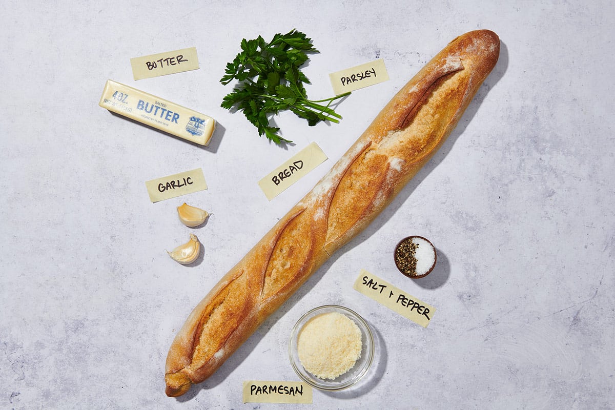 Baguette, butter, parsley, and other ingredients for garlic bread.