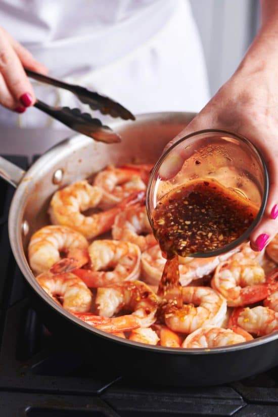 Woman pouring a Honey Garlic marinade over a pan of Shrimp.