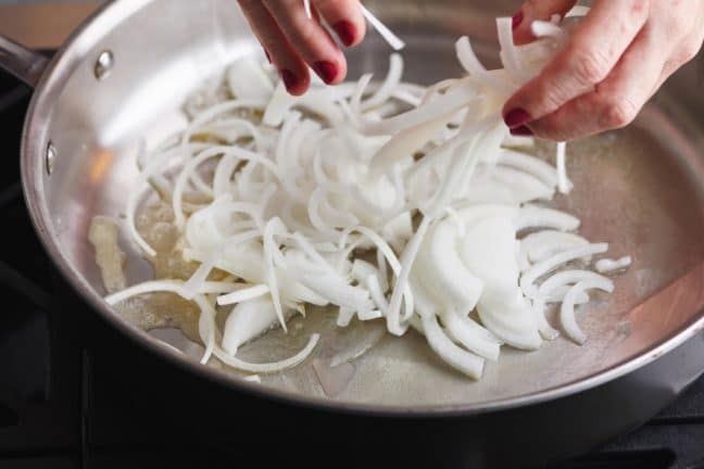 Woman tossing thinly-sliced onions into a pan.