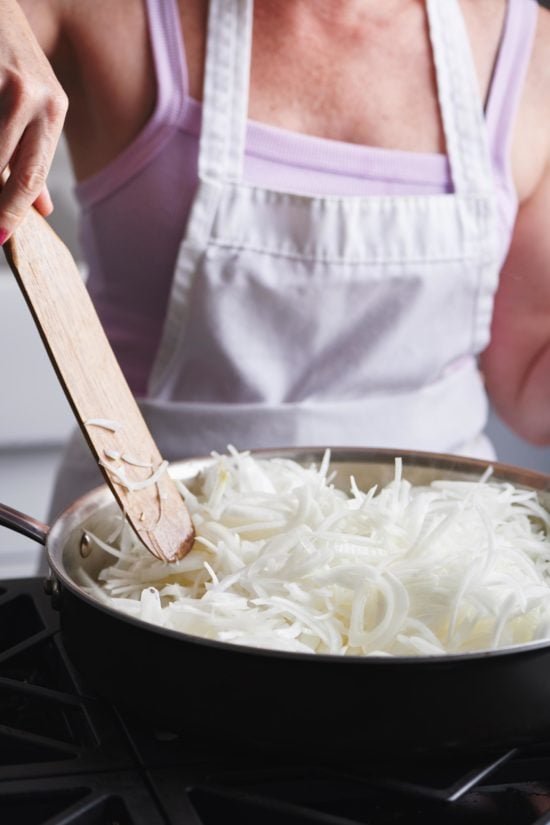 Woman stirring thinly-sliced Onions with a wooden spatula.