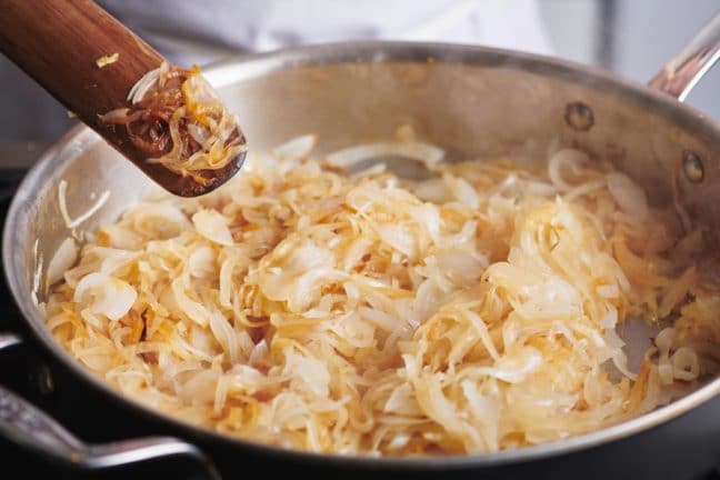 Wooden spatula over a pan of partially-Caramelizes Onions.