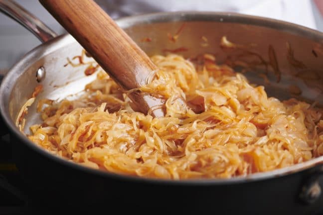 Pan of medium-brown onions being stirred by a wooden spatula.