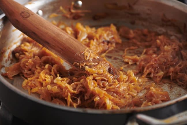 Wooden spatula in a pan of deeply-browned onions.