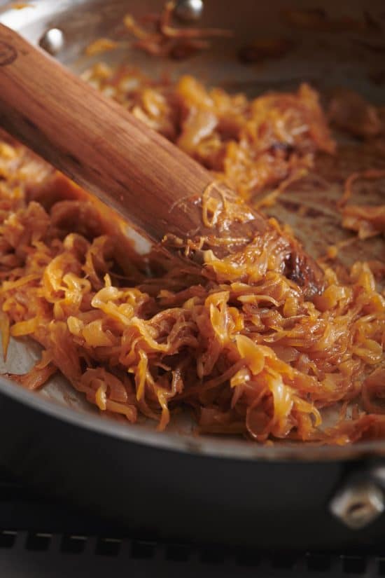 Wooden spatula stirring a pan of Caramelized Onions.