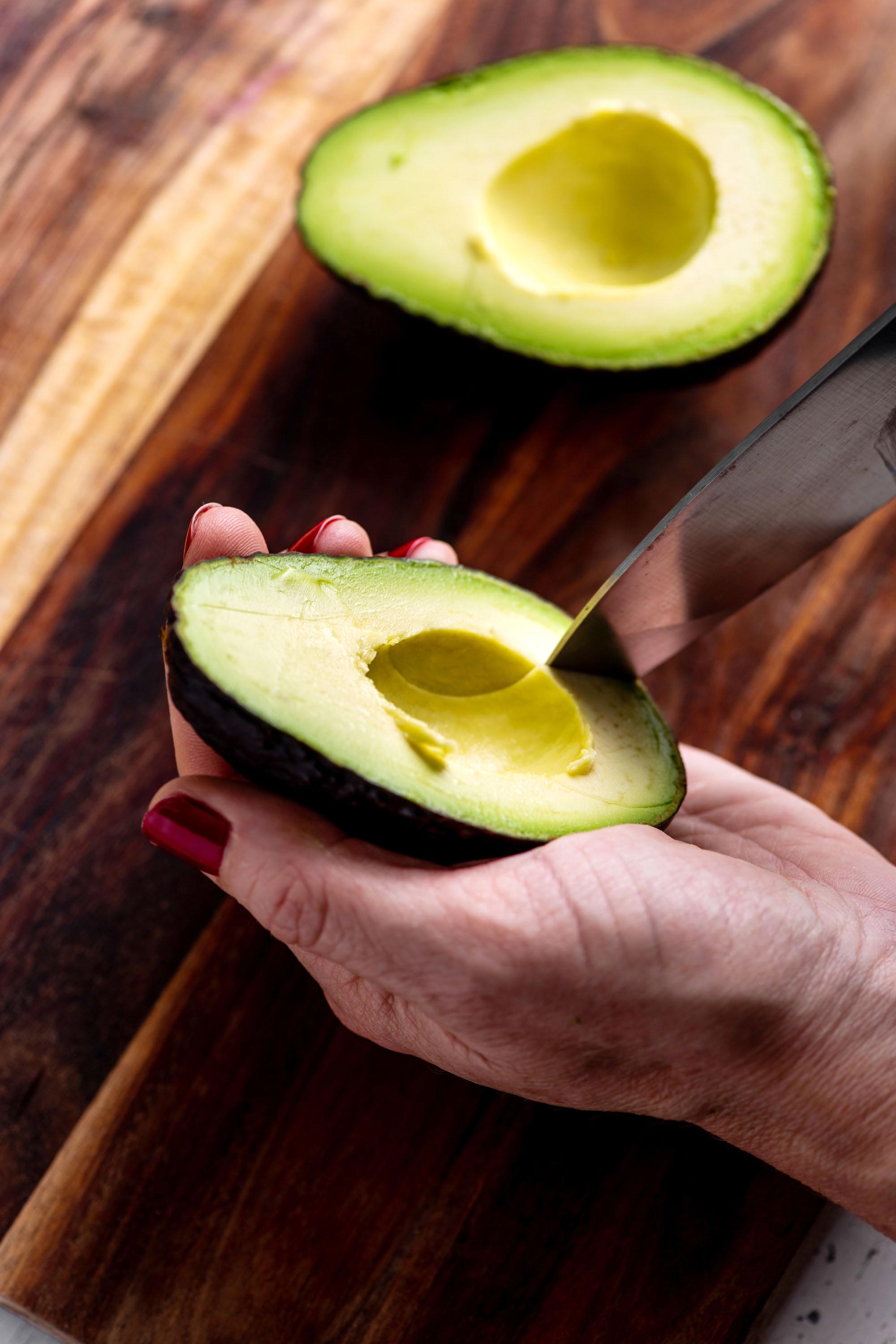 Woman cutting avocado in the shell with a knife.