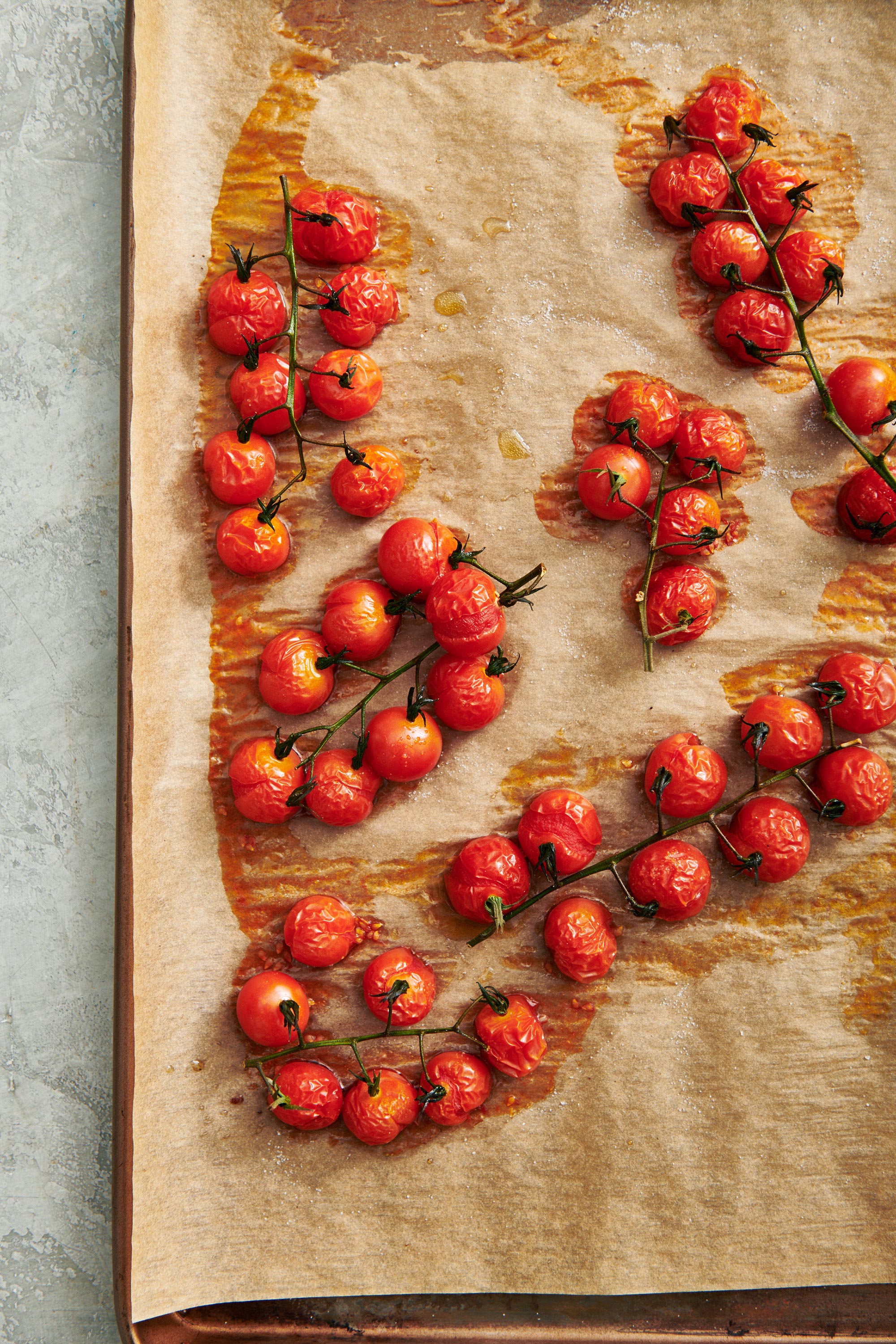 Roasted cherry tomatoes on baking tray covered with parchment paper.