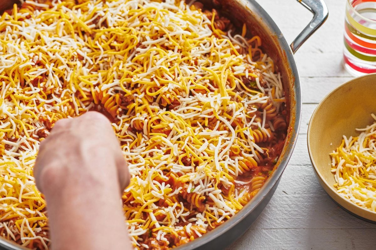 Cheese sprinkled on top of a skillet of Beefy Enchilada Casserole.