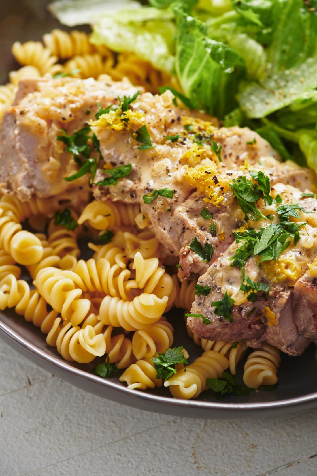 Slices of Creamy Mustard Pork Chops over noodles on a plate.