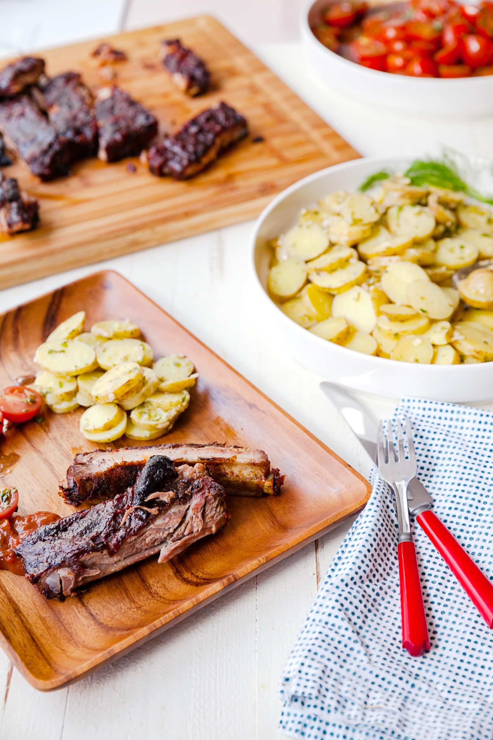 Oven Baked Cajun Sticky Ribs on table with potato and tomato salads.