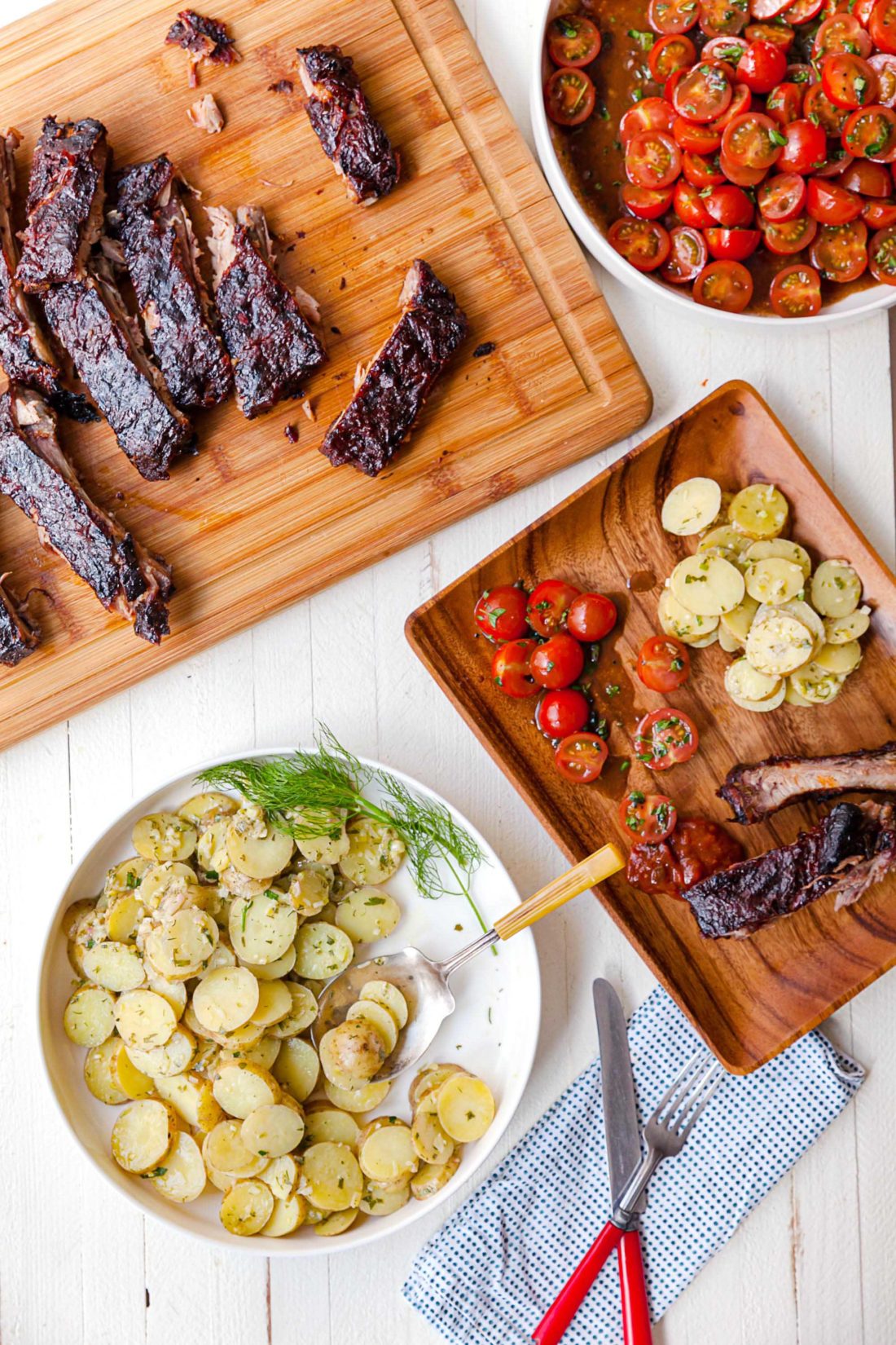 Cajun Sticky Ribs, potatoes, and tomatoes on a wooden plate.