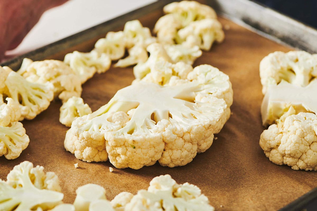 Cauliflower steaks and florets on a lined baking sheet.