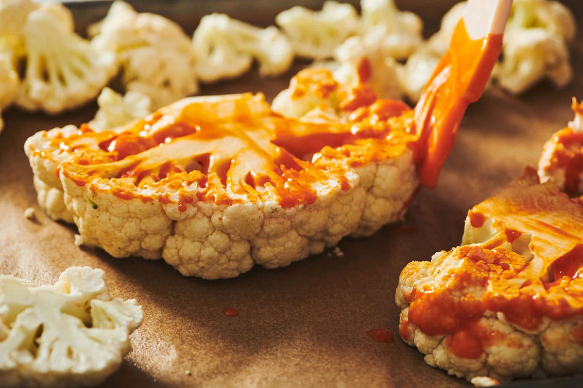 Woman brushing Buffalo sauce onto a Cauliflower Steak.