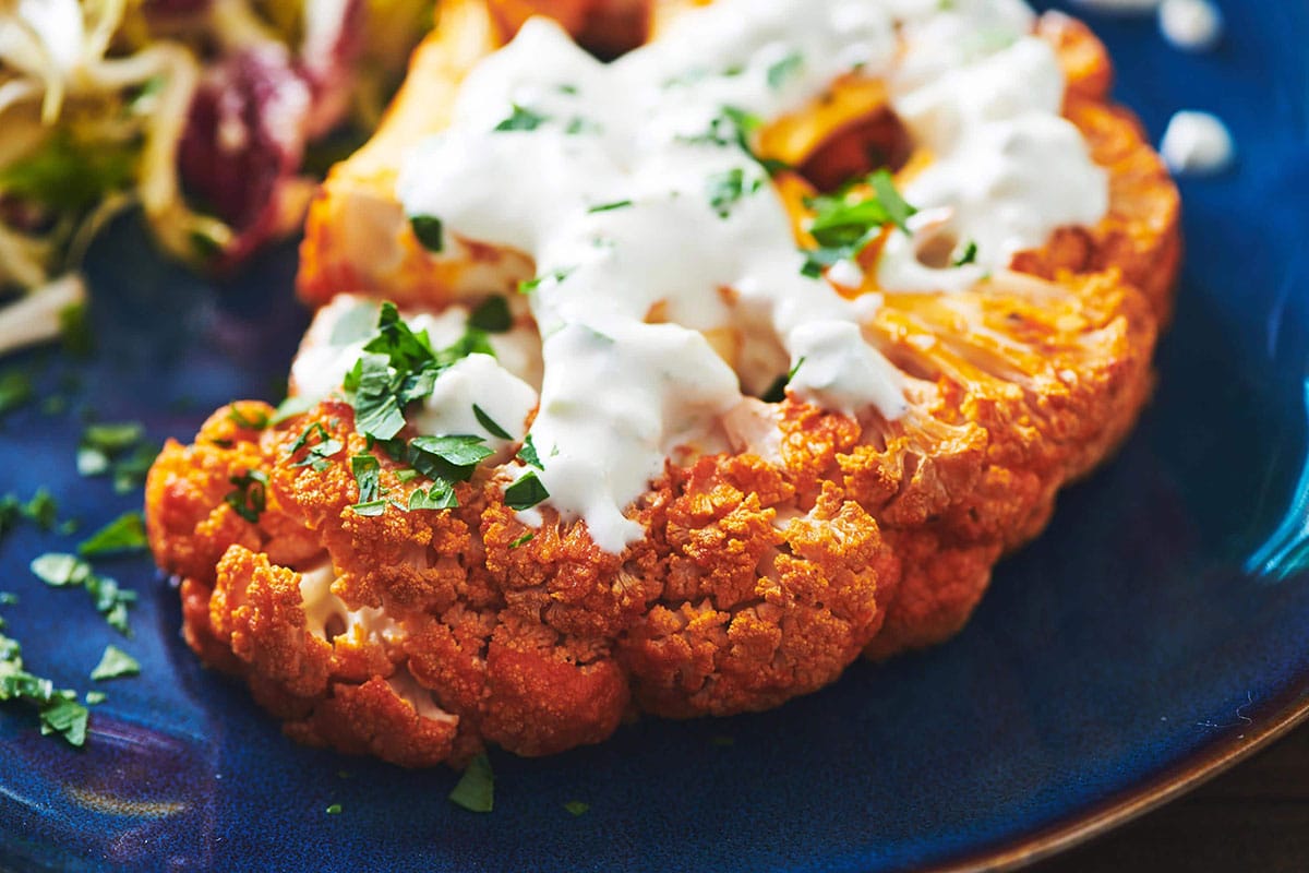Blue plate with a Roasted Buffalo Cauliflower Steak topped with Bleu Cheese Dip.