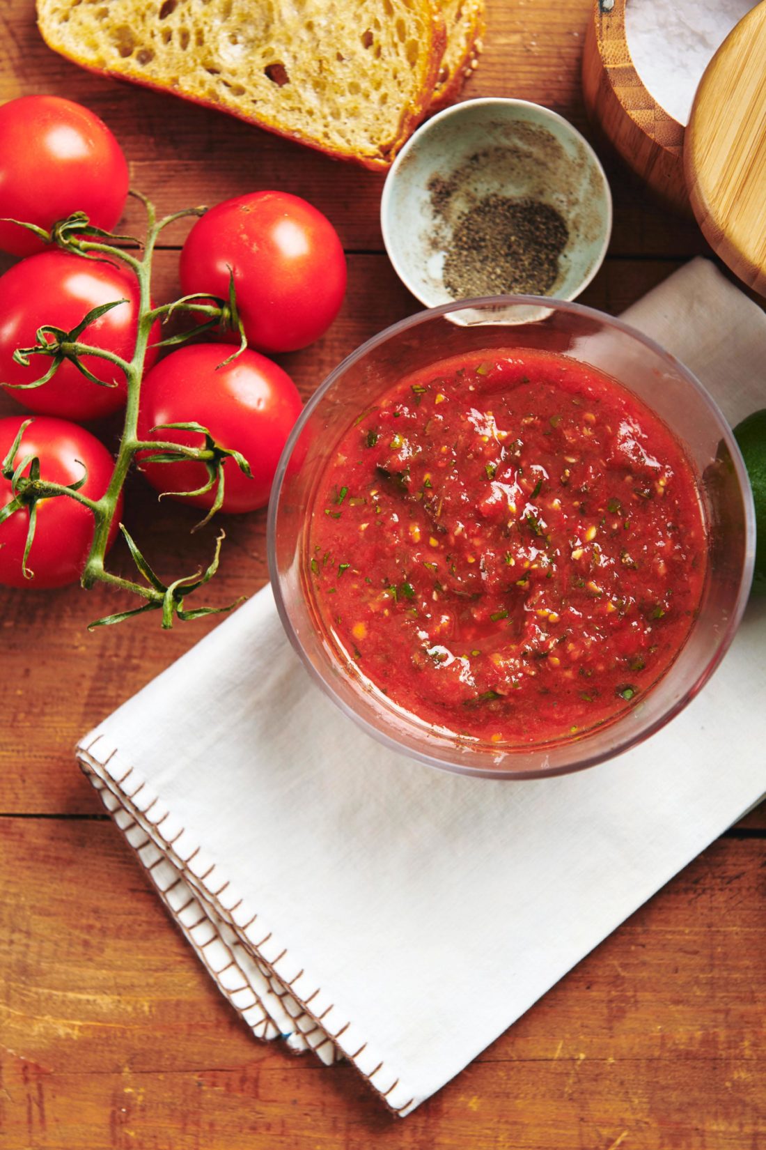 Bowl of Salsa Ranchera on a table with tomatoes and pepper.