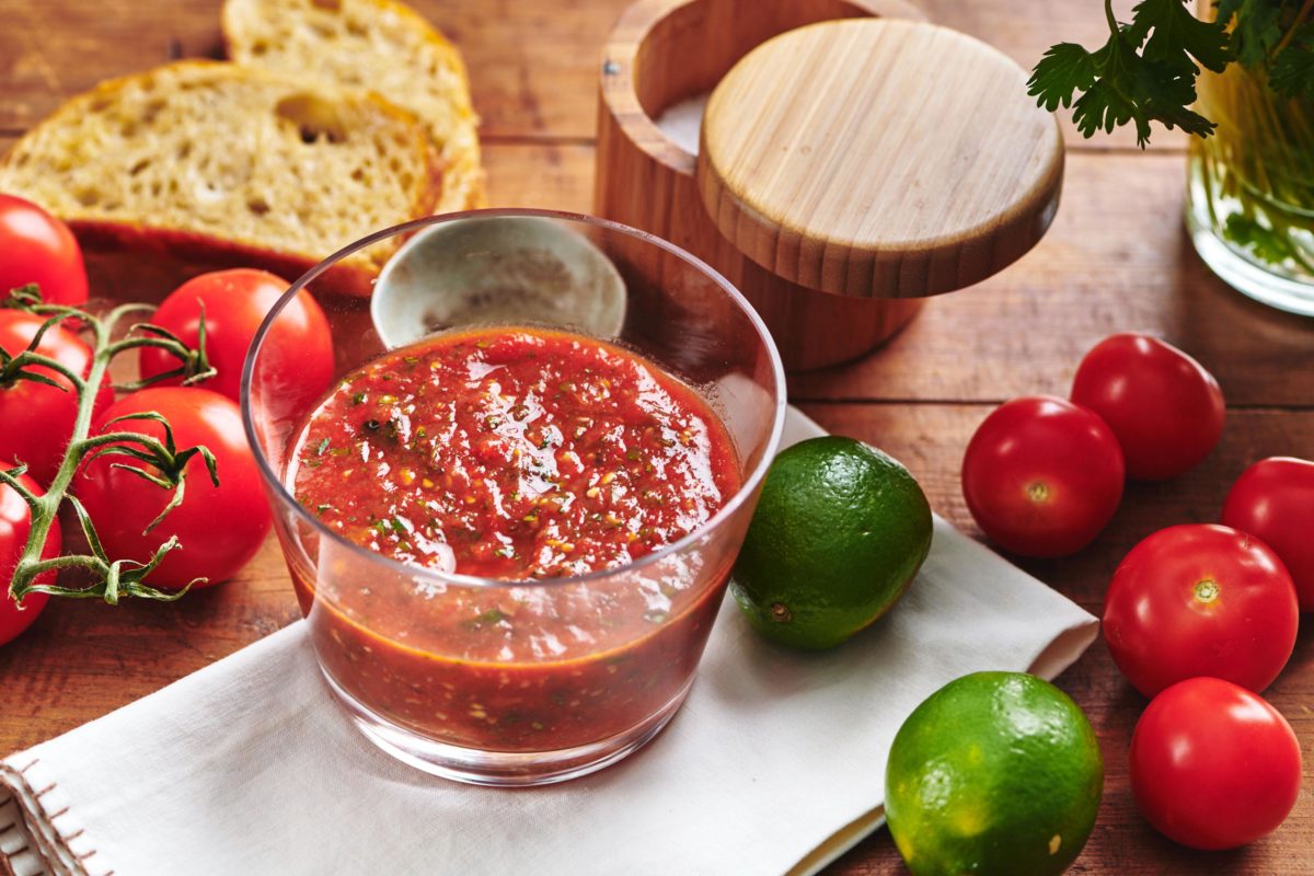 Salsa Ranchera on a table with tomatoes, limes, and bread.