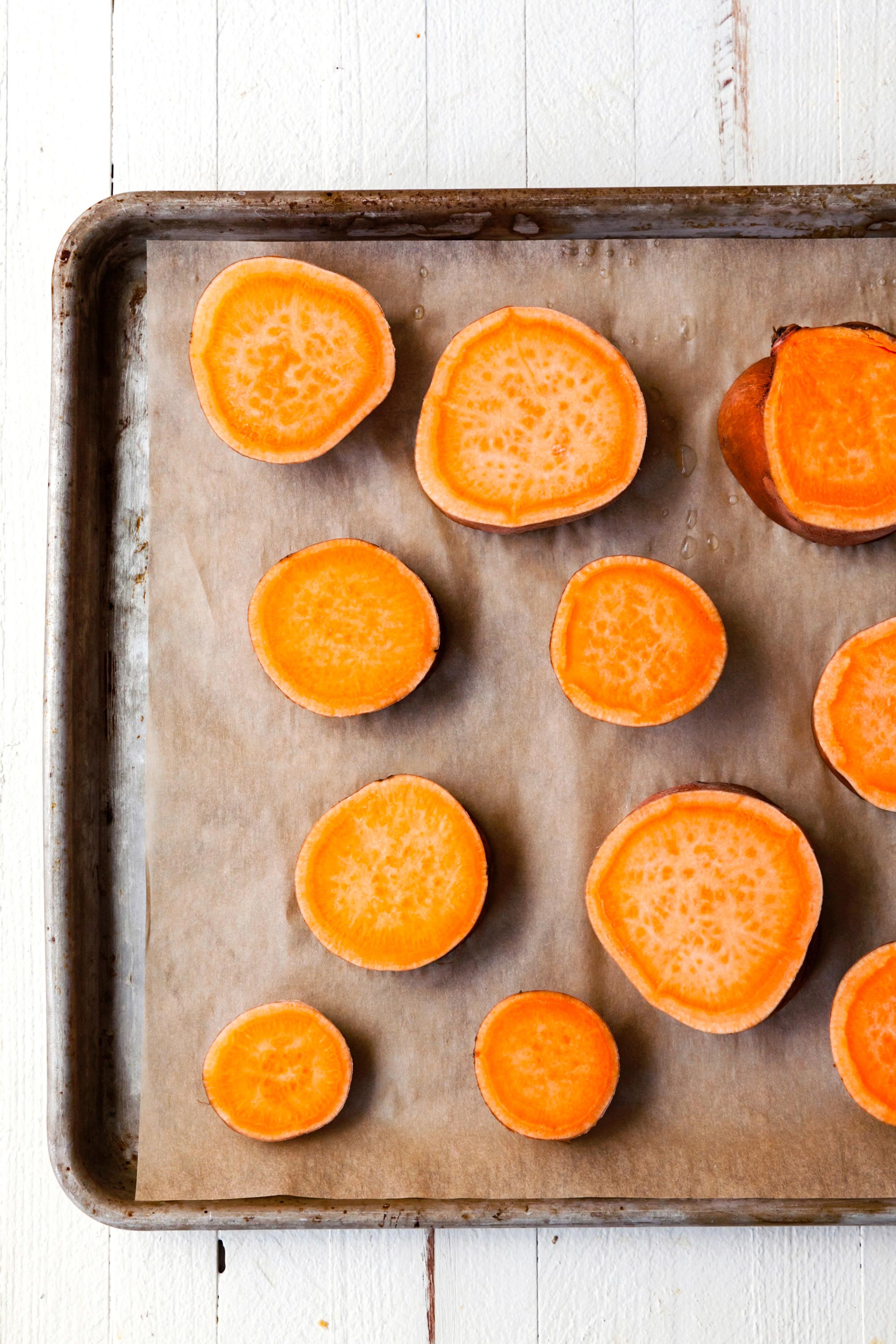 Slices of sweet potato on a parchment lined baking sheet.